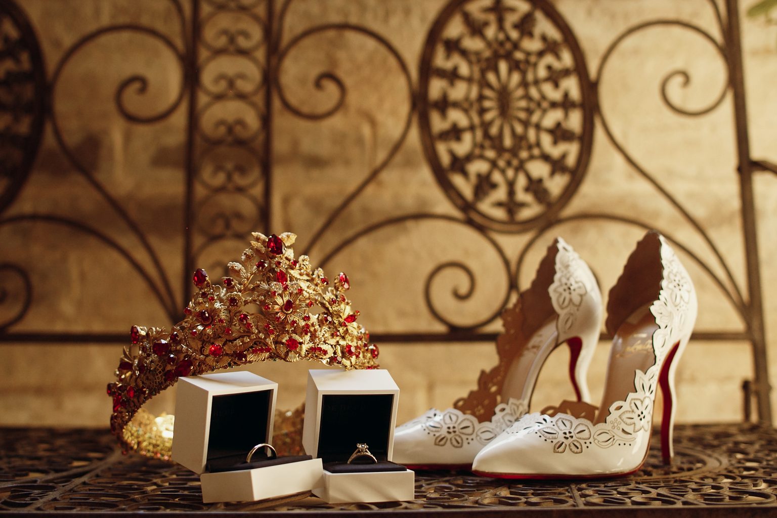 Golden crown with red stones, wedding rings and bride's shoes stand on steel bench